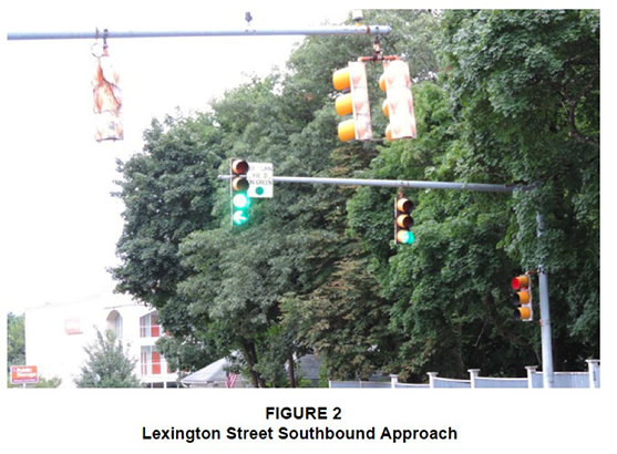 Figure 2. Figure 2 is titled "Lexington Street Southbound Approach.” It is a photograph taken from the perspective of a southbound driver approaching the traffic signal at the intersection. The traffic signal has a solid-green ball and, below it, a green left-turn arrow, indicating that a driver may make a protected left turn. 