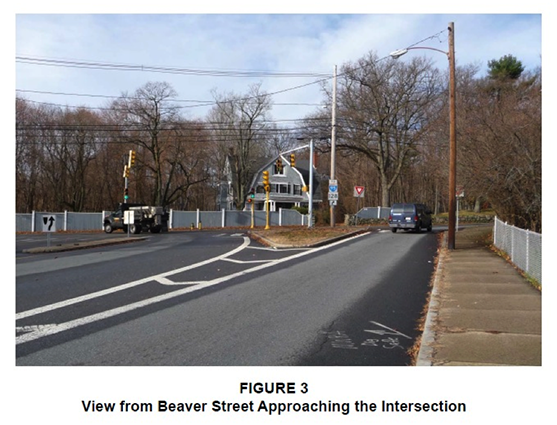 Figure 3. Figure 3 is titled “View from Beaver Street Approaching the Intersection.” It is a photograph taken from the perspective of a driver approaching the intersection. It shows that the two-lane approach is split by a triangular median. 