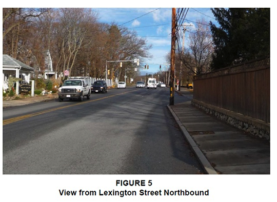 Figure 5. Figure 5, titled “View from Lexington Street Northbound,” is a photograph taken from the perspective of a driver traveling northbound. It shows the road ahead, some cars on the road, and some trees and houses at the sides of the road. 