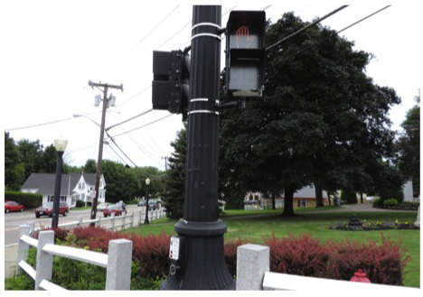 Figure 4, titled “Pedestrian Signal Facilities,” is a photograph of a pole on the sidewalk at the corner of the intersection that has a pedestrian push button at waist height and, higher up on the pole, two pedestrian crossing signals, one for each crosswalk.