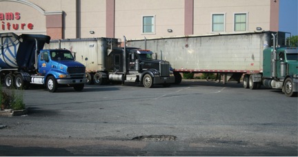 FIGURE 13. Adams Furniture Store on Second Street, Built in 2008: Scrap Metal Trucks Wait in Parking Lot with Large Pothole
Figure 13 shows three open-hopper semi-trailers of the largest allowable configuration waiting in a parking lot.
