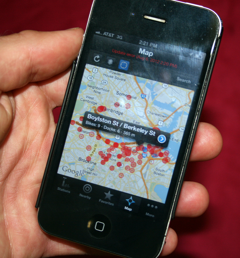 This is an image of a hand holding a smart phone showing a bikesharing app from Spotcycle.
