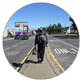 A person walking on the median in the middle of a highway.